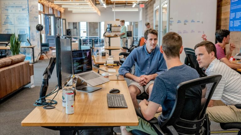 Profissionais reunidos diante de uma tela, representando trabalho colaborativo em tecnologia.